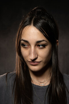 Joven modelo cauc&aacute;sica de pelo casta&ntilde;o oscuro, guapa, en fondo gris oscuro, mirando maliciosamente hacia un lado