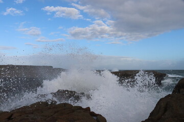 Sea waves impacts on this rock platform down below from the Norah head lighthouse in Central Coast Australia. Blue and white sky formations in the horizon.