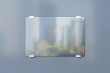 Realistic transparent glass frame with blurry city background on grey wall. Mockup