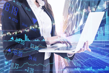 Online trading concept with businesswoman using laptop at skyscrapers background and digital screen with stock market financial graphs. Double exposure
