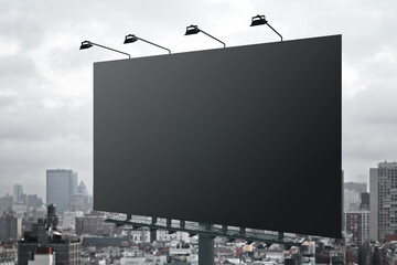 Huge blank black outdoor billboard with lights on top at city background. Mockup