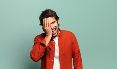 young handsome indian man laughing and slapping forehead like saying d’oh! I forgot or that was a...