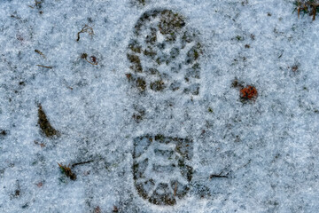 Boot footprint in the snow. green grass under the snow