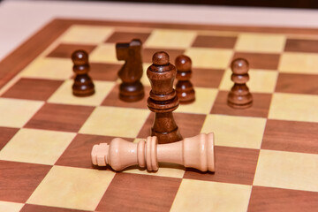 wood chess pieces on board game. brown vintage background. checkmate. the king is defeated by the queen
