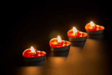 Four heart-shaped candles burning in the dark arranged in a diagonal line, copy space
