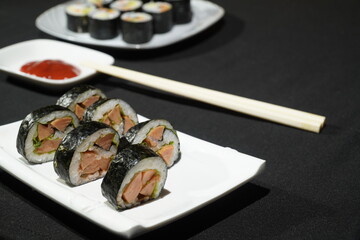 Sushi rolls, salad sauce, and chopsticks on black background. Popular Japanese cuisine