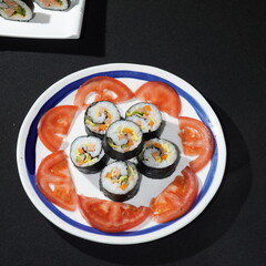 Sushi surrounded by sliced tomatoes in a plate on black background, Japanese restaurant recipe
