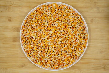 Dried corn kernels on round porcelain plate, top view, wooden background, healthy food