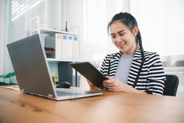 Attractive millennial Asian business woman using technology devices digital tablet and laptop computer for working research planning idea innovations business plans working at home office workstation