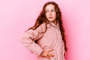 Little caucasian girl isolated on pink background looks aside smiling, cheerful and pleasant.
