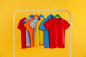 Rack with stylish children clothes on yellow background
