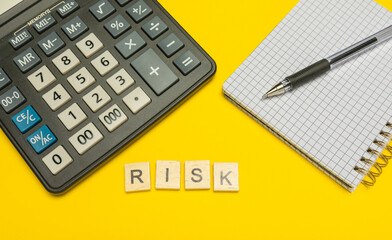 Word risk made with wood letters on yellow background and modern calculator with pen and notebook....