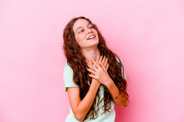 Little caucasian girl isolated on pink background laughing keeping hands on heart, concept of happiness.