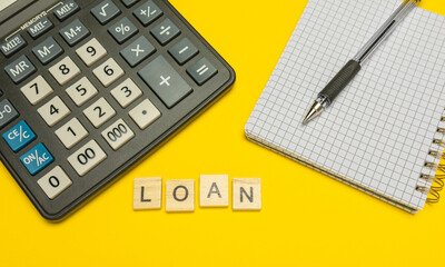 Word loan made with wood letters on yellow background and modern calculator with pen and notebook....