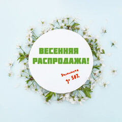 Text in russian SPRING SALE. SAVE UP TO 50%. Round frame with spring flowers. Flowers on cherry tree branches in form of wreath on blue background. Leaf pattern.