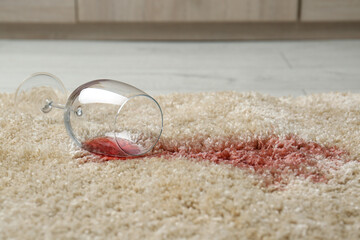 Overturned glass and spilled red wine on soft carpet
