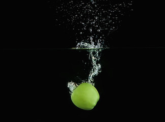 Ripe green apple falling down into clear water with splashes against black background