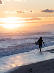 Fototapeta premium Surfer on the beach running during the sunset