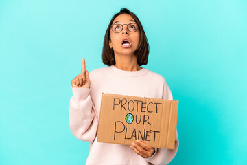 Fototapeta na wymiar Young hispanic mixed race woman holding a protect our planet cardboard pointing upside with opened mouth.