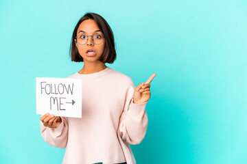 Young hispanic mixed race woman holding a follow me placard pointing to the side