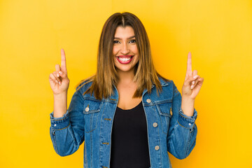 Young indian woman isolated on yellow background indicates with both fore fingers up showing a...