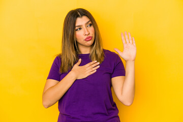 Young indian woman isolated on yellow background taking an oath, putting hand on chest.
