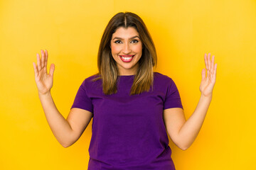 Young indian woman isolated on yellow background holding something little with forefingers, smiling and confident.