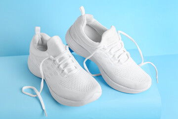 Stylish white sports shoes on light blue background