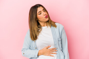 Fototapeta premium Young indian woman isolated on pink background touches tummy, smiles gently, eating and satisfaction concept.