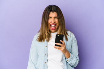 Fototapeta premium Young indian woman holding a phone isolated screaming very angry and aggressive.