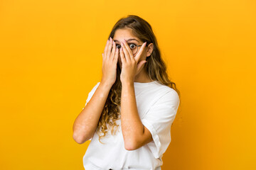 Young caucasian woman blink through fingers frightened and nervous.