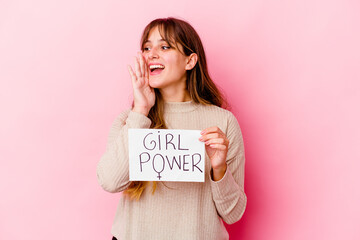 Young caucasian woman holding a girl power placard isolated on pink background shouting and holding palm near opened mouth.