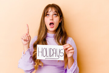 Fototapeta na wymiar Young caucasian woman holding a Holidays placard isolated pointing upside with opened mouth.