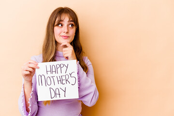 Fototapeta na wymiar Young caucasian woman holding a Happy mothers day placard isolated looking sideways with doubtful and skeptical expression.
