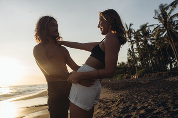 The man holds the woman by the waist as she swerved backwards and put her hand on his shoulder against the backdrop of the ocean and palm trees. High quality photo