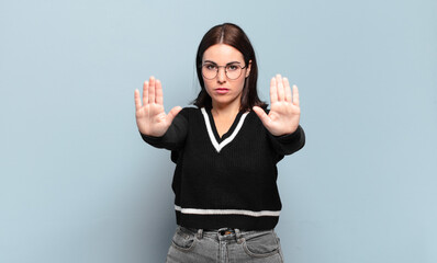 young pretty casual woman looking serious, unhappy, angry and displeased forbidding entry or saying stop with both open palms