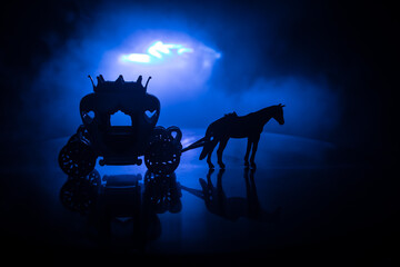 Little carriage with horse miniature on table. Creative decoration on dark toned foggy background.