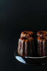 Caneles de bordeaux - traditional French sweet dessert serve with tea or coffee in dark tone on black background.