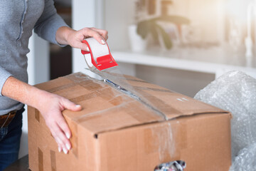 Young woman is sealing a cardboard box with tape packed for moving