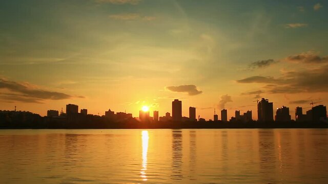 Time-lapse, lake view in city at sunrise, reflection of rising sun and buildings on water 