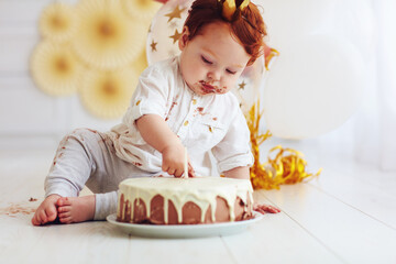 cute baby boy poking finger in his first birthday cake