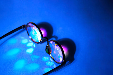 The kaleidoscope glasses in the black frame in the rays of light on a blue background. There is...