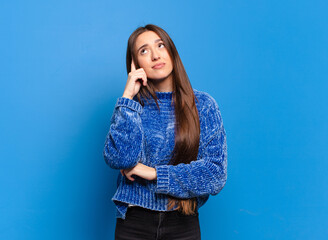 young pretty casual woman with a concentrated look, wondering with a doubtful expression, looking...