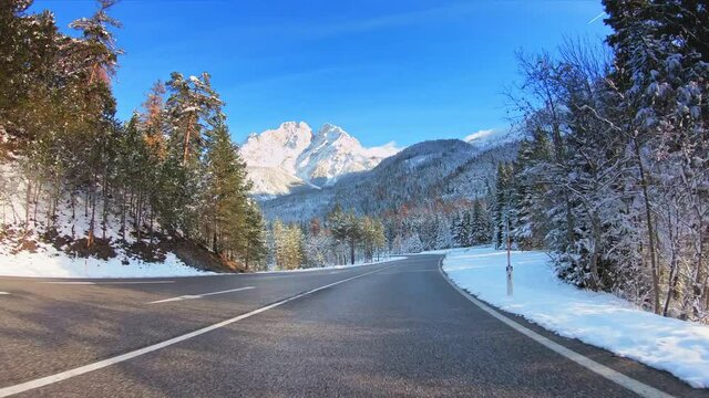 Beautiful winter landscape POV vehicle drive, forest evergreen trees, mountains snow peaks, asphalt road and sunny blue sky, car travel gopro point of view