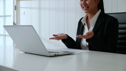Businesswoman sit on the table in office, She's having a video call meeting. He gestures to...