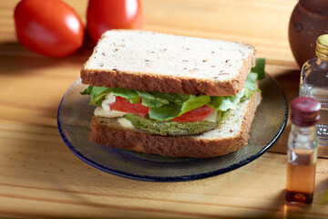 A closeup from above of vegan sandwich with medallion of spinach and carrot, tomato, lettuce, vegan cheese and mayonnaise on rustic wooden table.