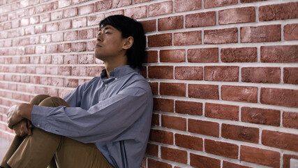 Depressed young man sitting on floor against a wall