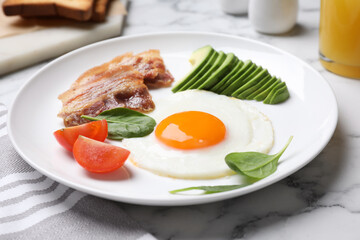 Tasty breakfast with fried egg, bacon and avocado served on white marble table, closeup