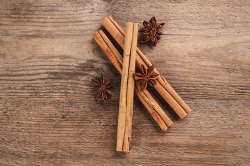 Aromatic cinnamon sticks and anise on wooden table, flat lay