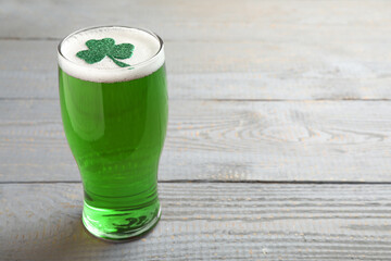 Glass of green beer with clover leaf on grey wooden table, space for text. St Patrick's Day celebration